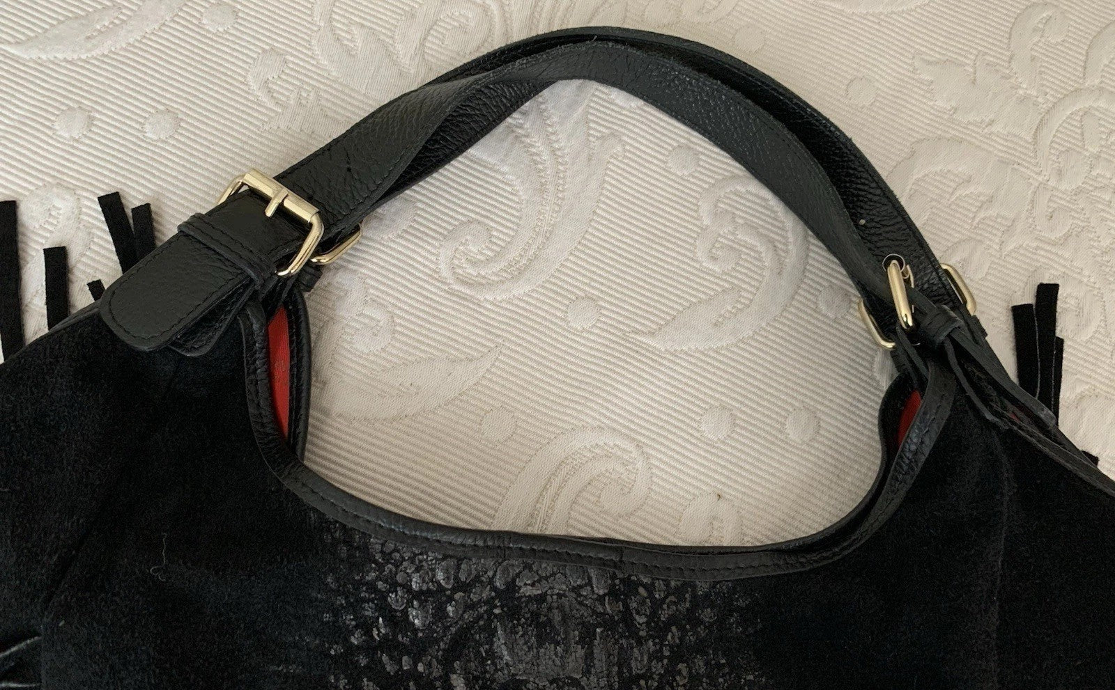 Detailaufnahme des oberen Bereichs der Tasche mit dem Schulterriemen und der goldfarbenen Schnalle.