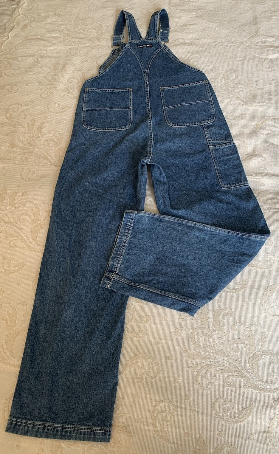 Rückansicht einer blauen Tommy Hilfiger Latzhose mit Logo am Rücken mit geknicktem Bein